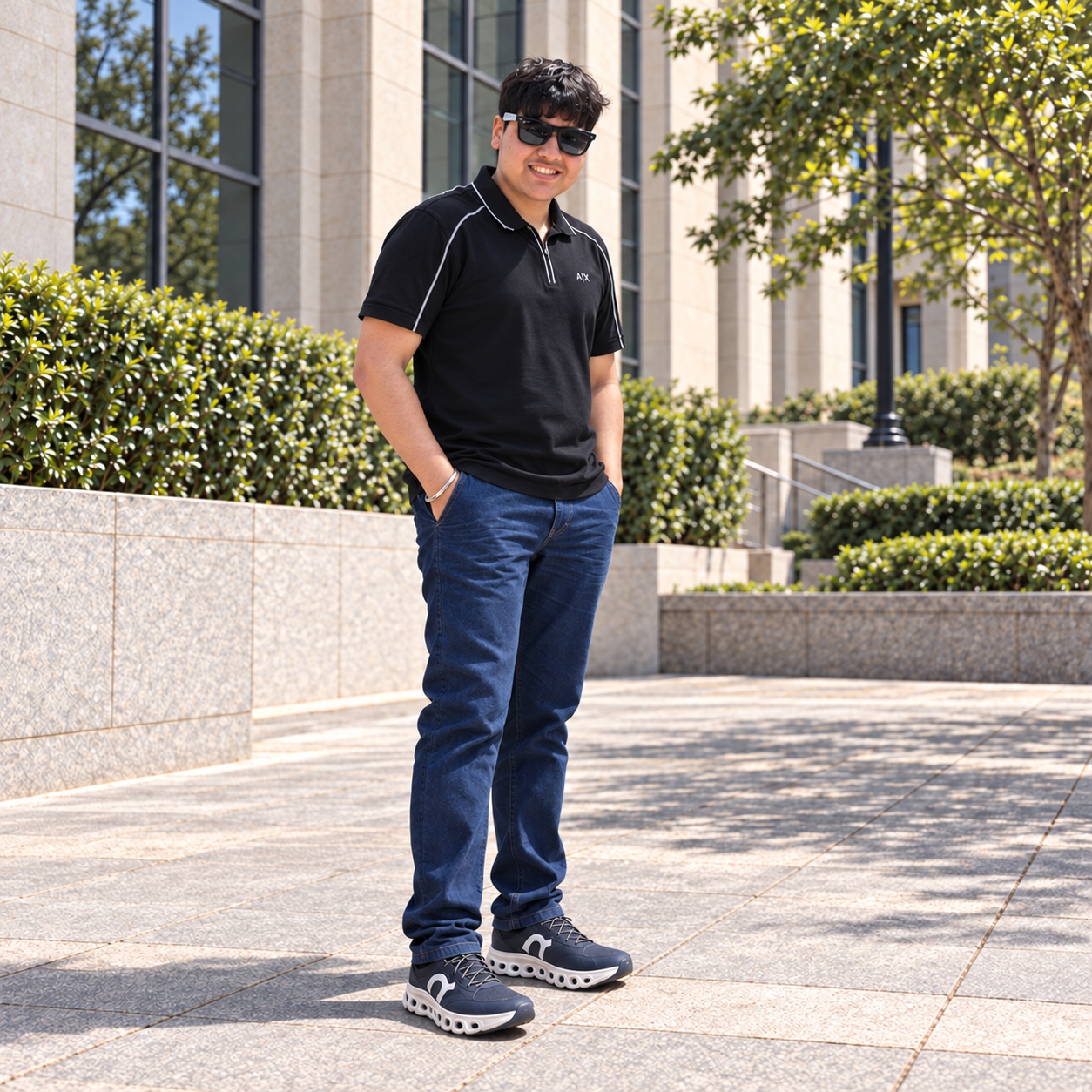 Krish Gandhi standing outdoors, wearing sunglasses, a black polo shirt, and jeans